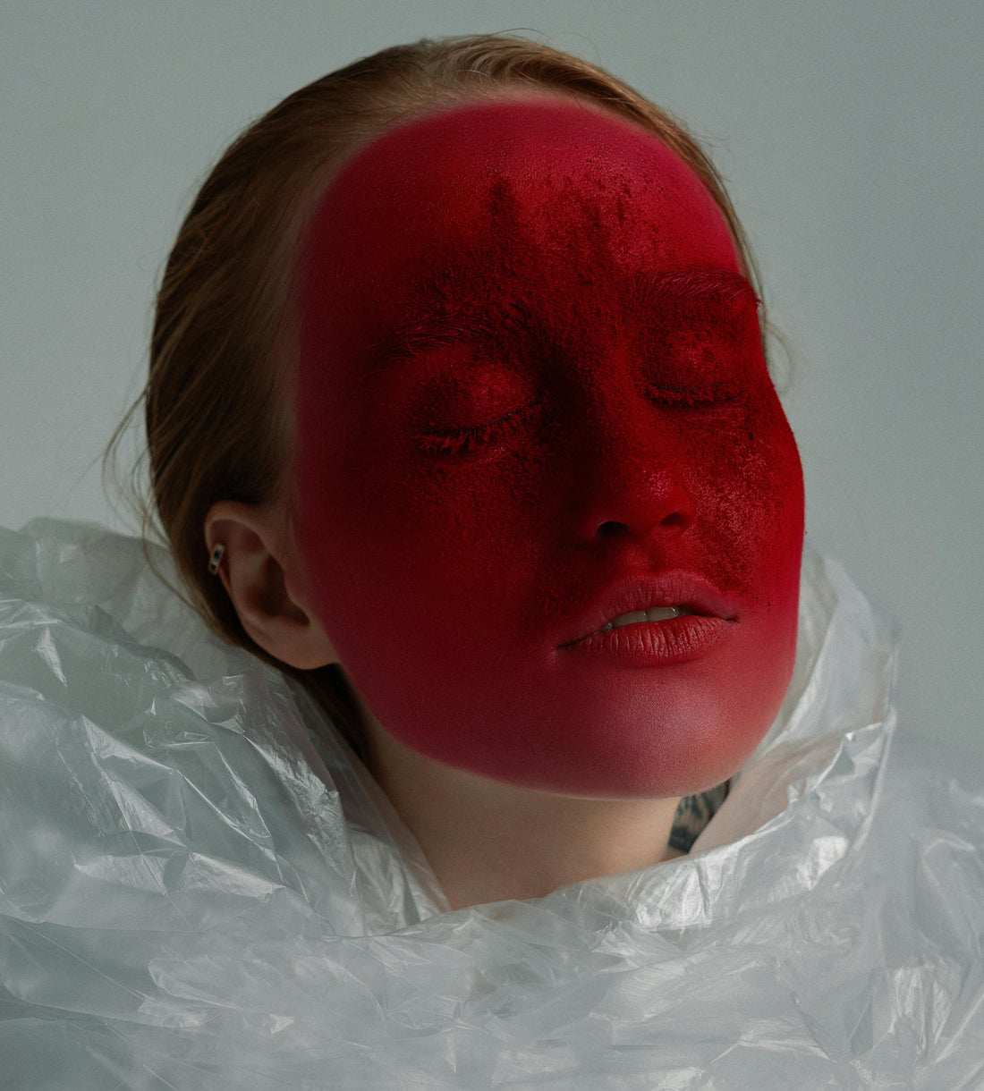 es una mujer con los ojos cerrados y la cará pintada de rojo, simulando la sangre y conceptualizando el período menstrual en las mujeres y el sexo