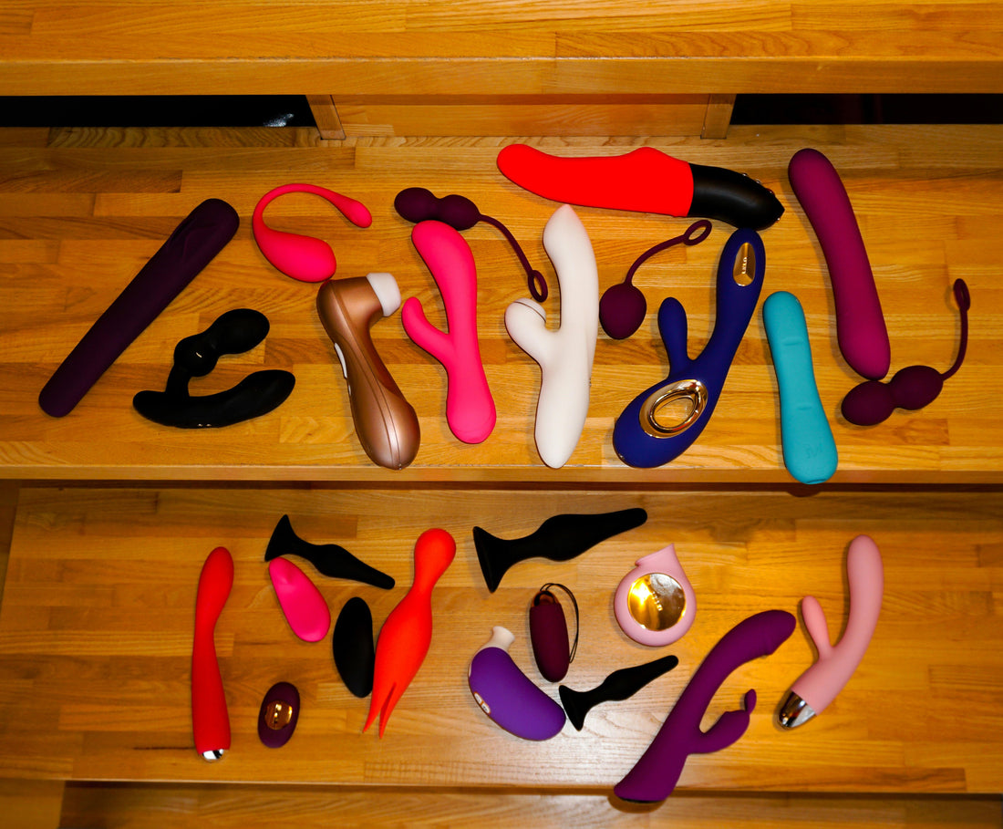 Variedad de juguetes sexuales (succionadores de clítoris, vibradores, plug anal, consoladores), de varias formas, tamaños y colores cobre unos escalones de madera